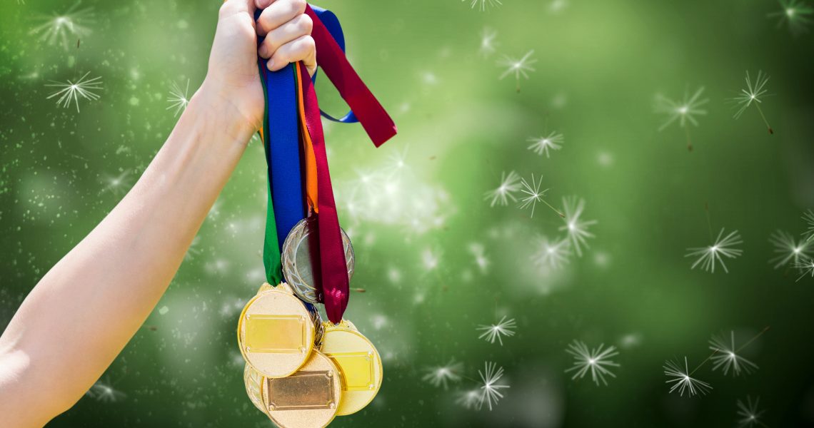 composite of hand holding medals over nature background